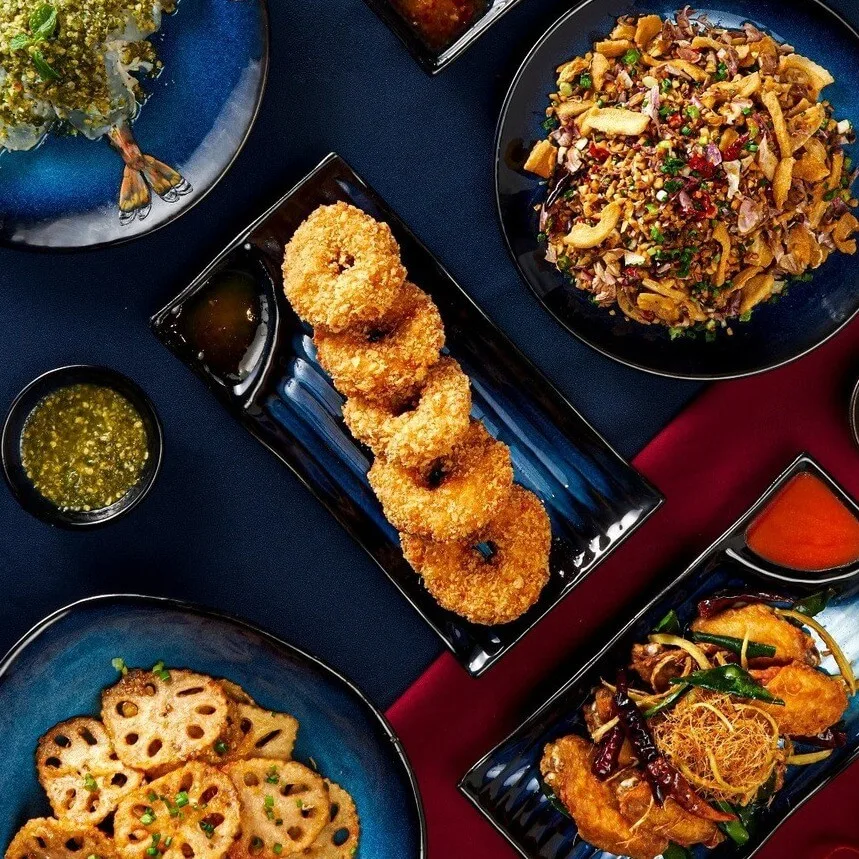 Thai stir-fried noodles, crispy calamari rings, and lotus root tempura served on dark charcoal-blue stoneware