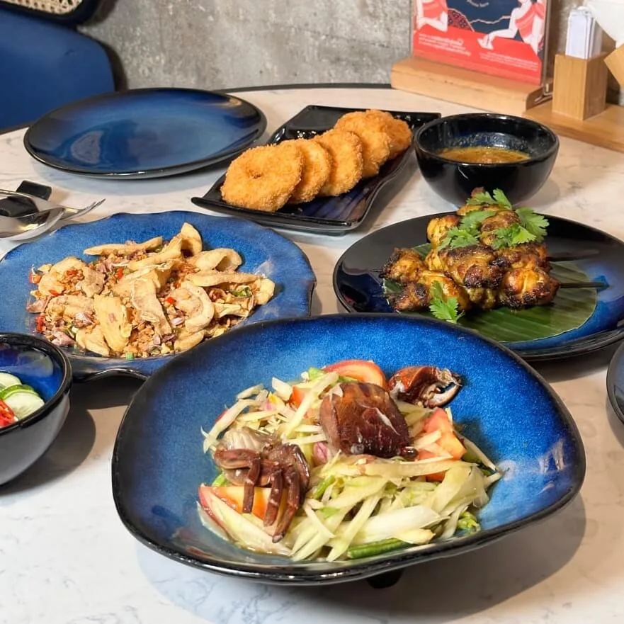 Zesty Som Tum green papaya salad with salted field crab, paired with chicken satay skewers and crispy donut prawn cakes