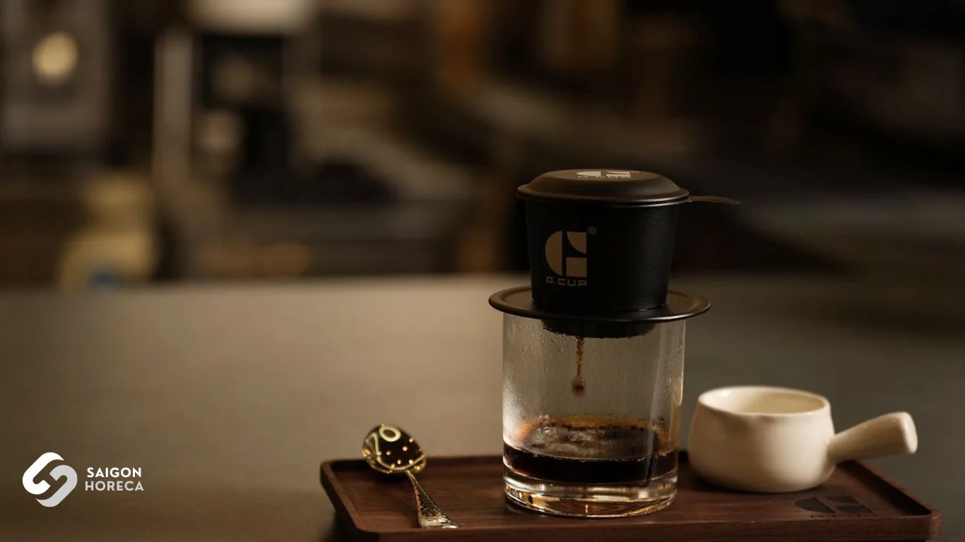 Black aluminum phin dripper with G.Cup logo extracting into glassware on a wooden tray
