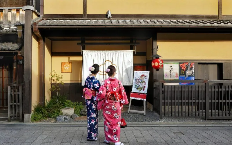 Two women in elegant kimono standing before the traditional Kyoto-style Grand Marble boutique storefront