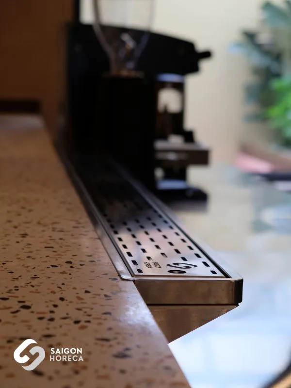 Detailed view of the recessed stainless steel drain trough flush-mounted into the terrazzo counter—ensuring clean drainage and rapid sanitation at the barista station
