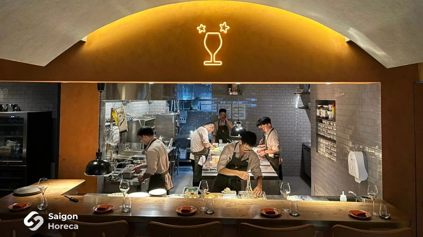 Artisanal oak bar counter and arched open kitchen pass-through illuminated by neon wine glass signage at Little Bear Thao Dien