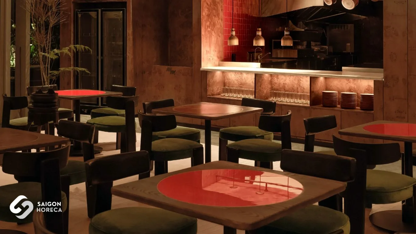 Mam Mam dining hall featuring red lacquer-finish wooden tables and olive green velvet seating, with the open kitchen station custom-built by Saigon Horeca in the background