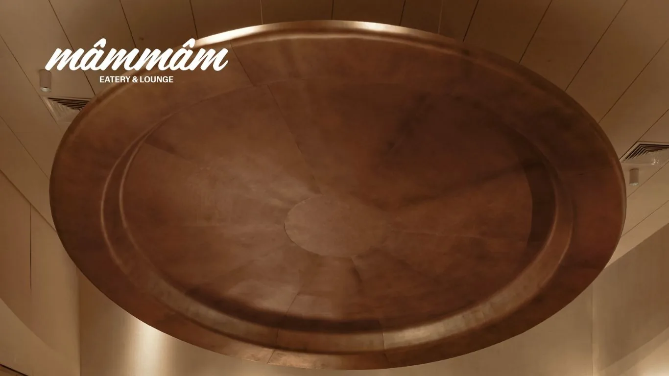 Circular decorative ceiling installation finished in antique copper clad within natural wood paneling with recessed ambient downlights at Mam Mam