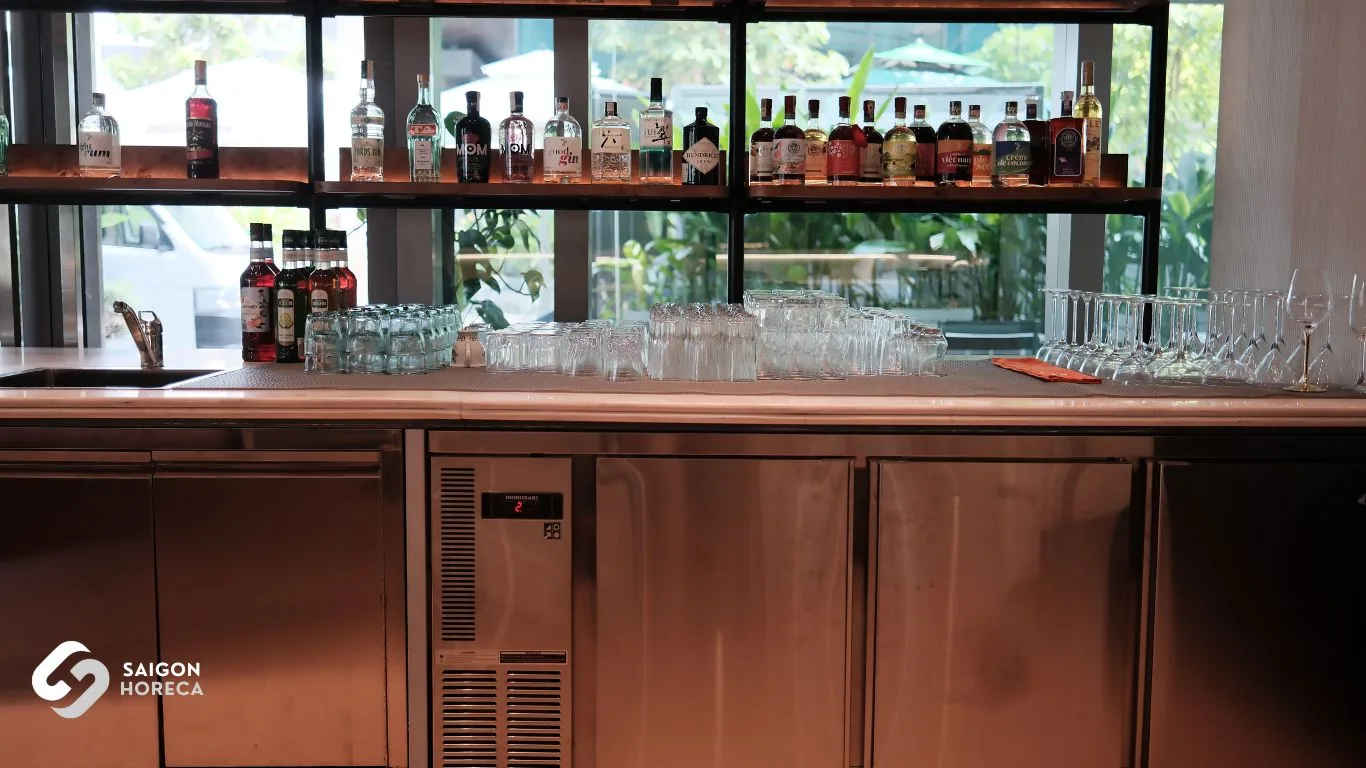 Mam Mam lounge cocktail bar with under-counter stainless steel chillers, sparkling glassware, and illuminated liquor display shelving