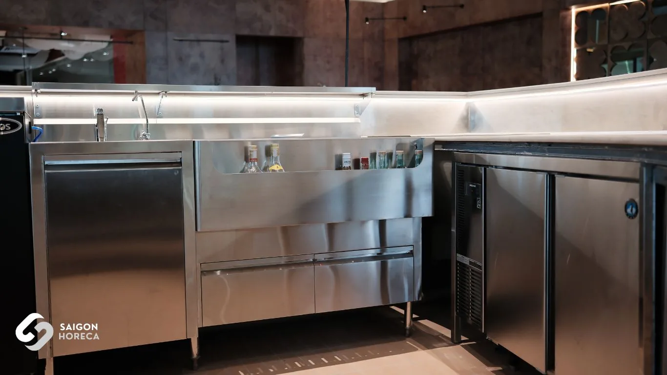 L-shaped stainless steel mixology station featuring wash sinks, bottle rails, and under-counter refrigeration engineered by Saigon Horeca at Mam Mam