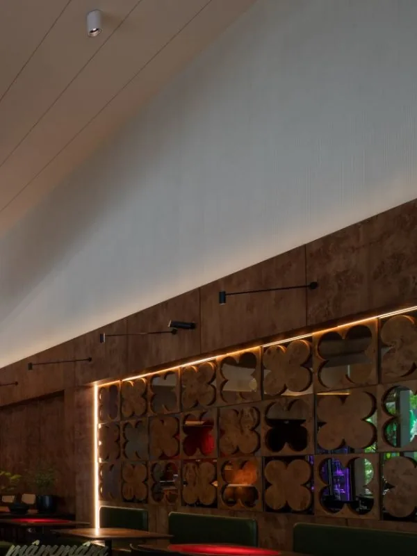 Decorative partition featuring four-petal floral motifs with backlit warm LED accents in the Mam Mam dining room, combined with white pitched ceilings and plush green seating