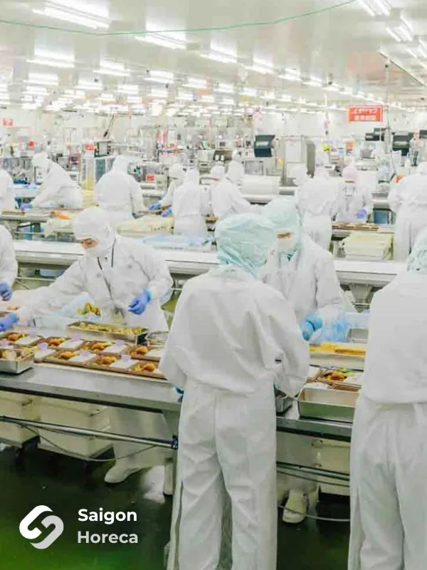 Operators in full cleanroom PPE arranging fried items onto trays along stainless steel conveyors in Nichiyo's food processing facility