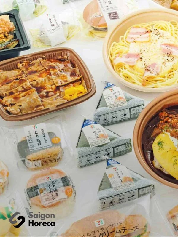 Assorted ready-to-eat Japanese meals: packaged onigiri rice balls, spaghetti carbonara, teriyaki glazed meats, and Japanese curry rice