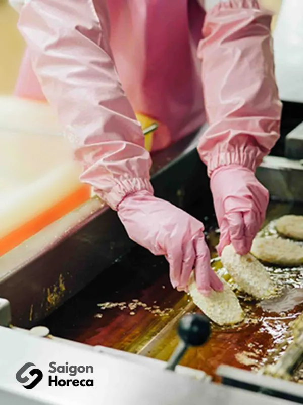 Kitchen operator wearing safety gloves deep-frying breaded cutlets in heavy-duty commercial stainless steel deep fryers at Nichiyo canteen