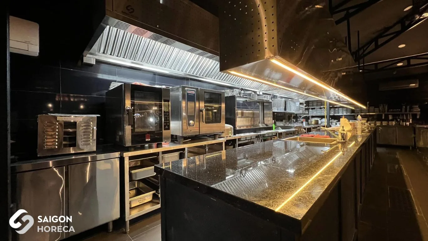 Upgraded stainless steel kitchen line at Sol Kitchen & Bar District 7 post-renovation: EKA convection oven, RATIONAL combi oven, stainless steel exhaust hood with integrated LED lighting, and natural stone kitchen island with LED perimeter accents.