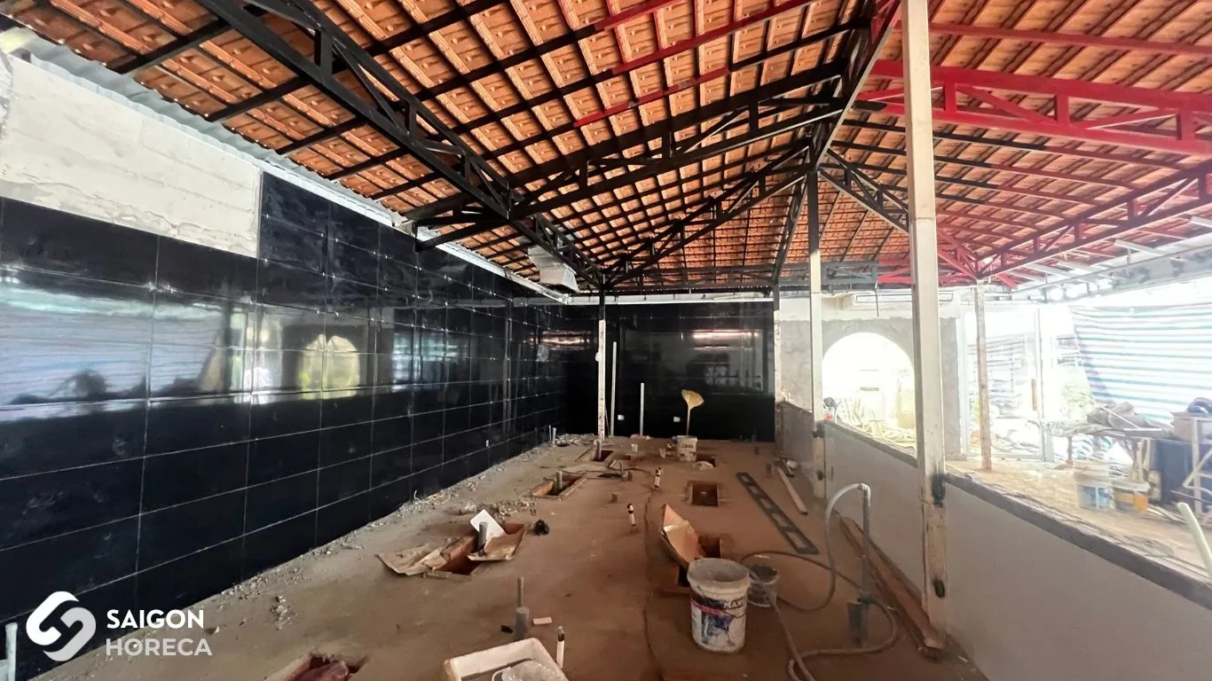 Active renovation construction under tiled roof with black tiled walls and concrete flooring amidst building materials at Sol Kitchen & Bar District 7.
