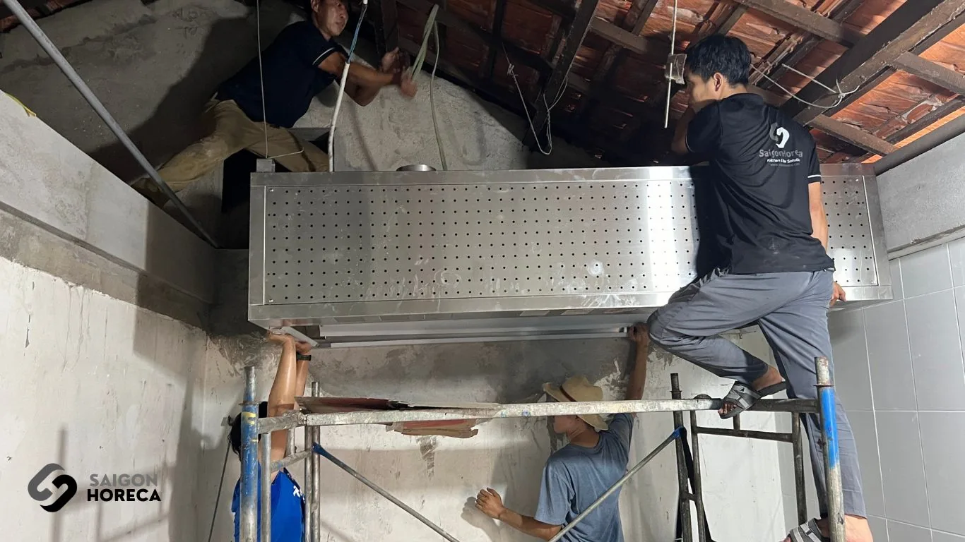 Saigon Horeca technicians mounting the 2-meter stainless steel hood to the ceiling during kitchen fit-out at Sol Kitchen & Bar District 7.