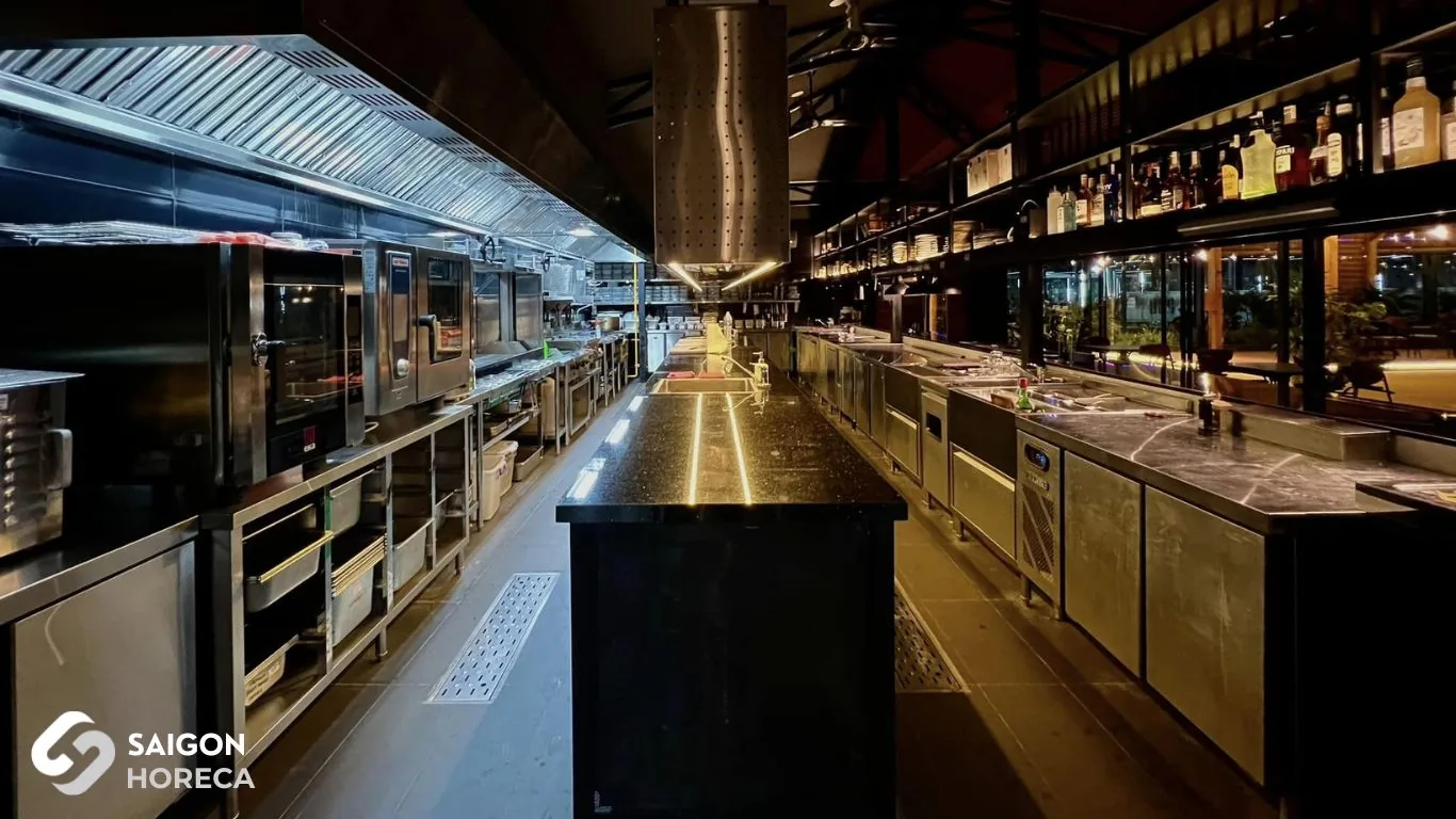 Overview of completed commercial stainless steel kitchen and bar counter at Sol Kitchen & Bar District 7: combi oven, undercounter chillers, exhaust hood system, and granite kitchen island.