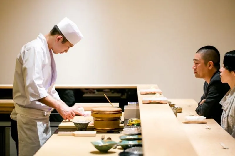 Sushi chef performing and serving guests live at Roka Fella's Omakase counter.