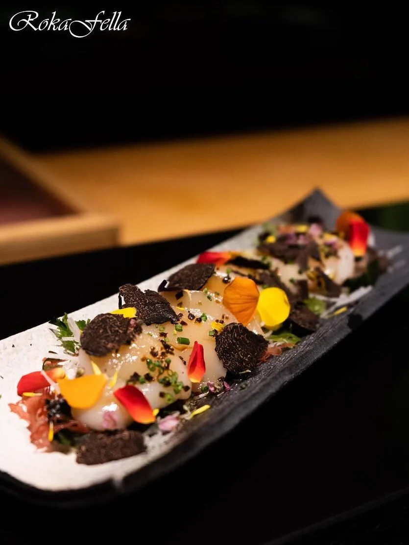 Lightly torched scallop sashimi garnished with shaved black truffle and edible flower petals at Roka Fella.