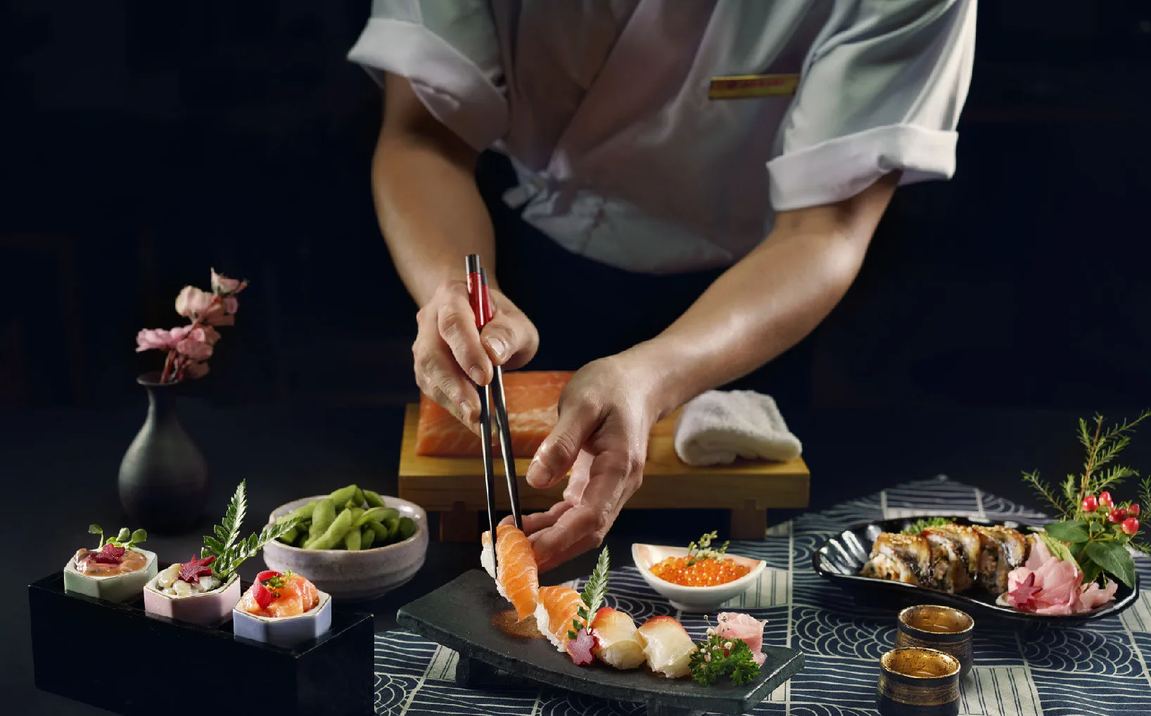 Chef delicately placing fresh salmon slice atop nigiri sushi on Roka Fella's Omakase presentation tray.