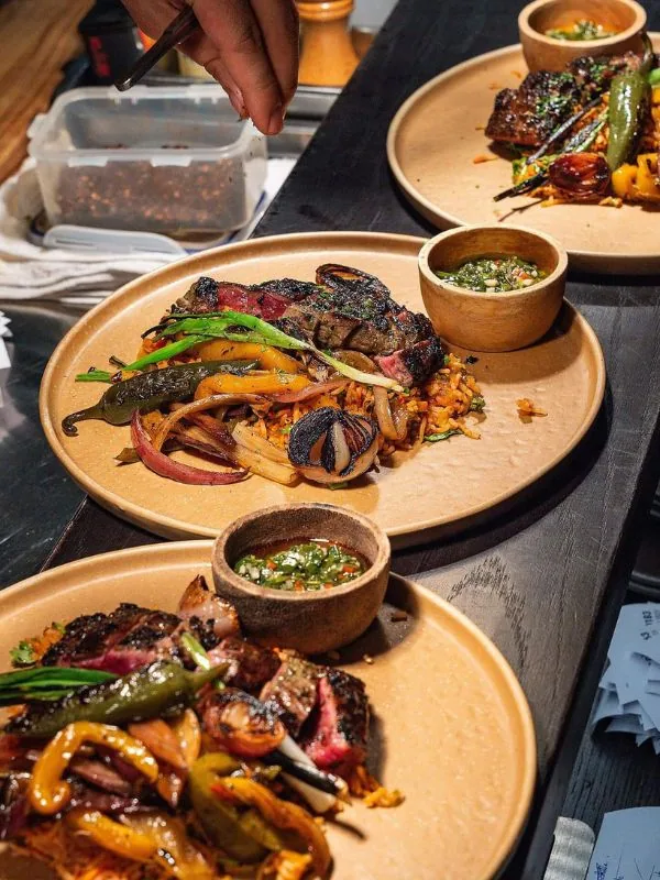 Sliced grilled beef over Latin red rice, served with charred peppers, caramelized onions, and house chimichurri sauce at Sol Kitchen & Bar