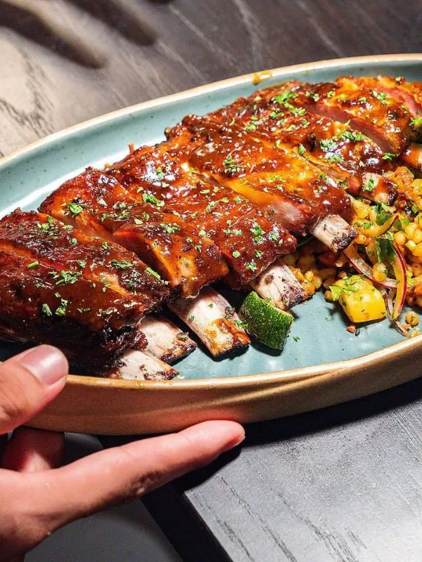 Glazed BBQ pork ribs coated in rich reddish-brown sauce, accompanied by seasoned vegetable couscous at Sol Kitchen & Bar