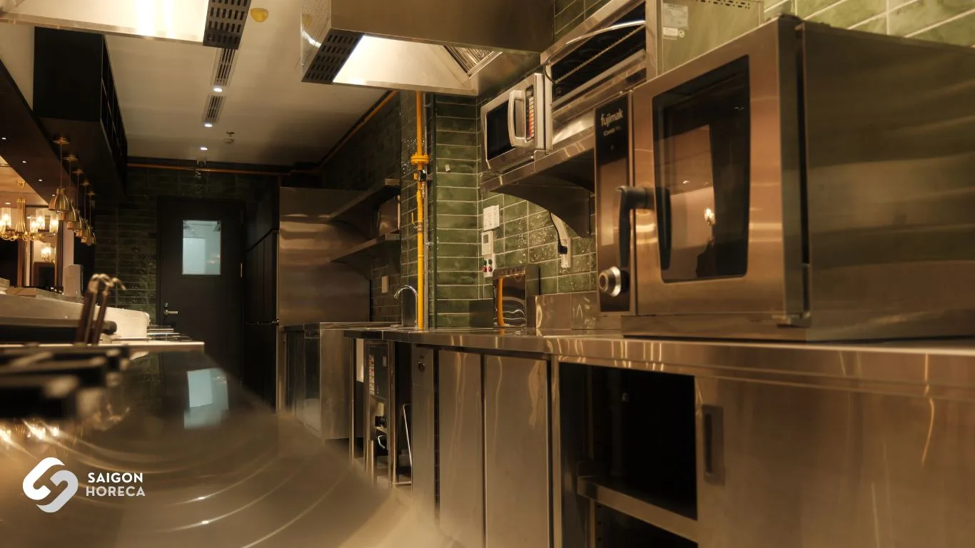 Commercial stainless steel prep counters and deep sink battery beneath vintage brass pendant lamps at The Royal