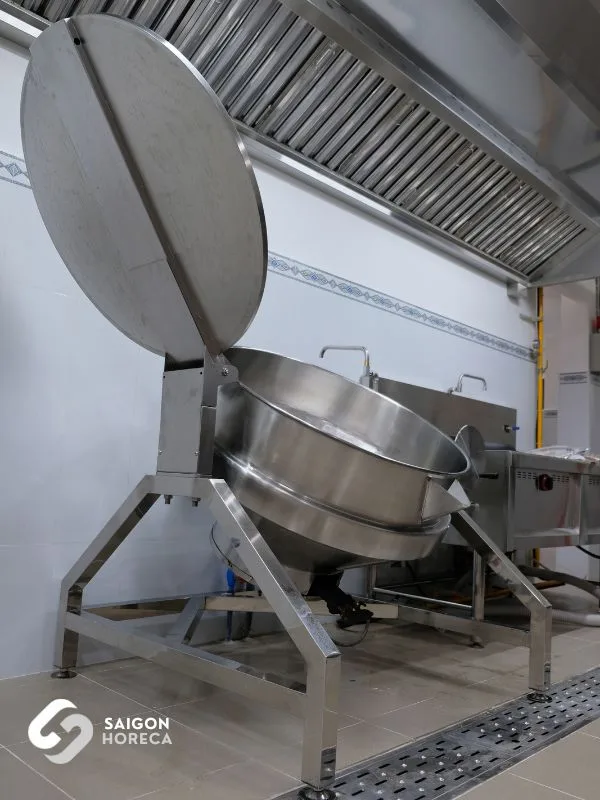 High-capacity stainless steel tilting kettle positioned beneath the exhaust hood at Trinh Vuong Kindergarten kitchen