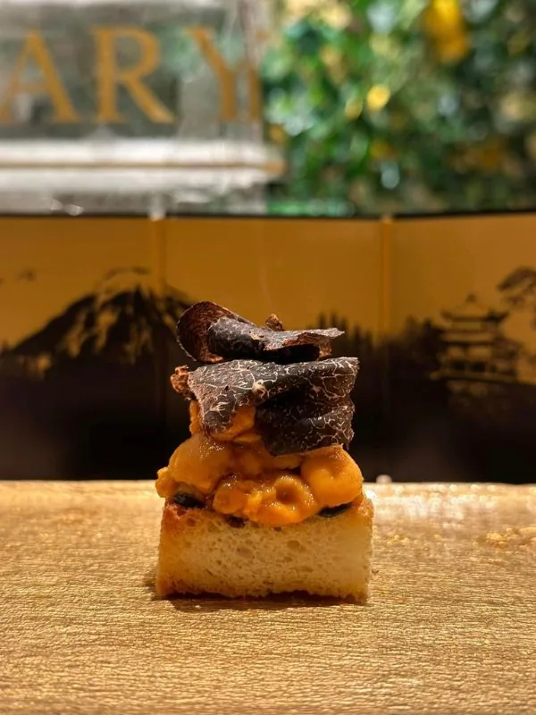 Crisp toasted brioche topped with fresh sea urchin (uni) and shaved black truffle against gold Mount Fuji screen