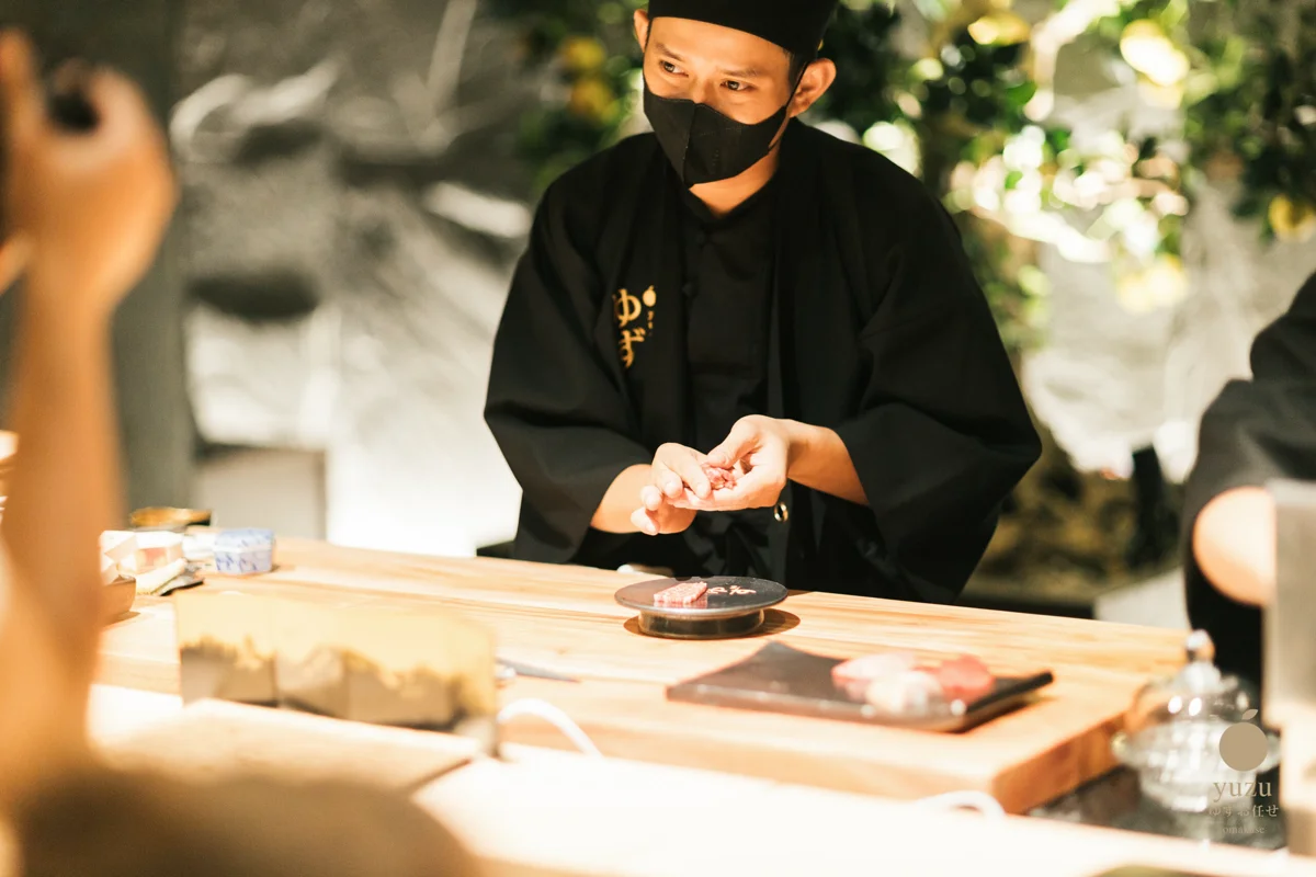Sushi artisan hand-crafting nigiri at the signature Hinoki wood counter of Yuzu Omakase